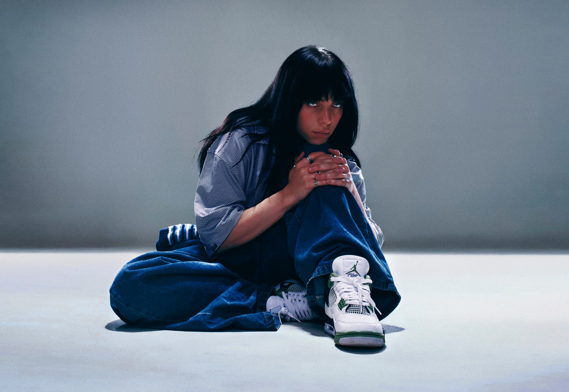 Billie Eilish seated in denim and Jordan sneakers