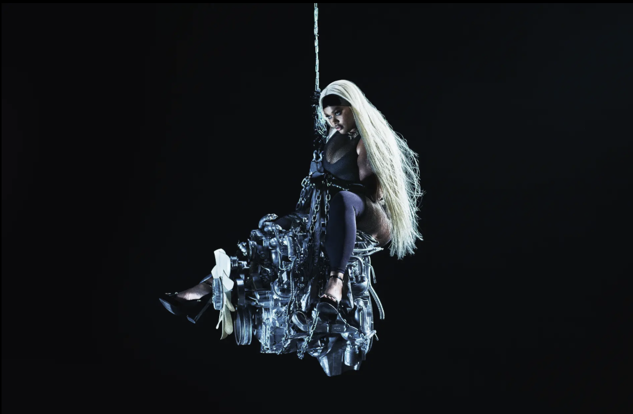 Savage x Fenty — figure seated on a suspended engine against black