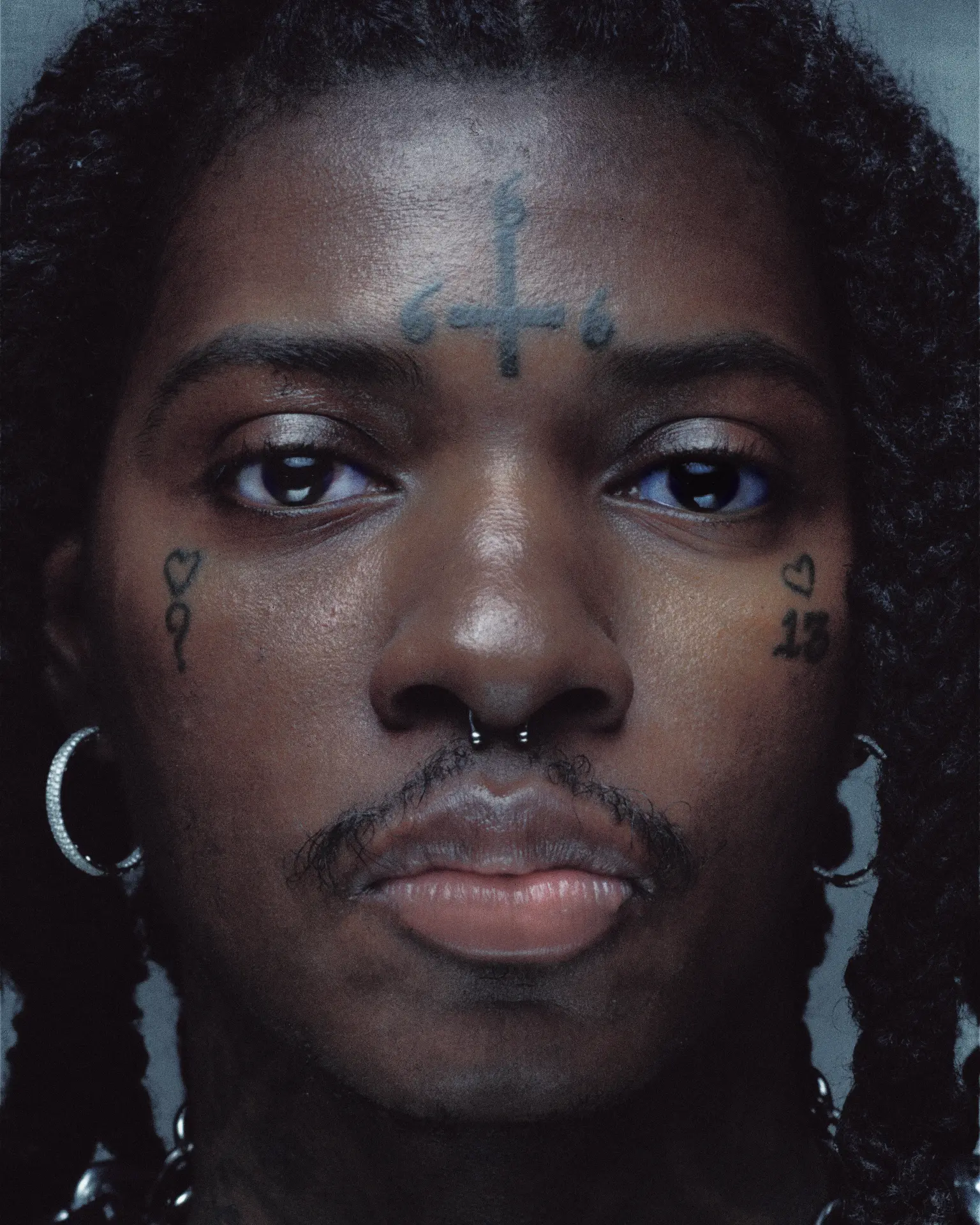 SahBabii close-up portrait with cross forehead tattoo and hoop earrings