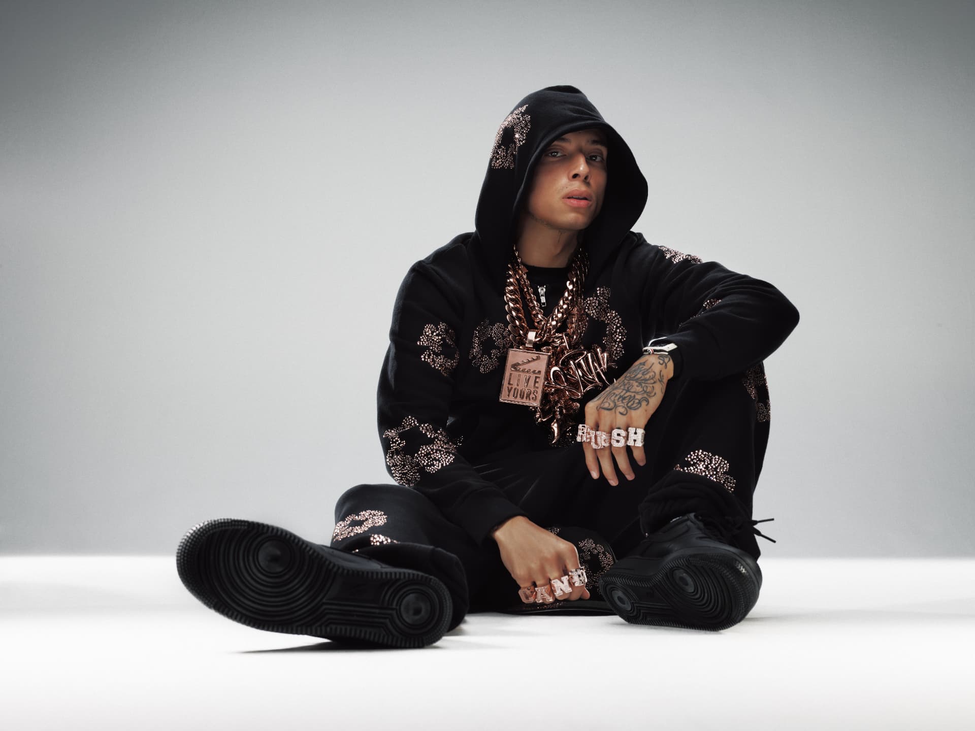 Central Cee — seated portrait in black hoodie and jewels showing CAN'T RUSH rings