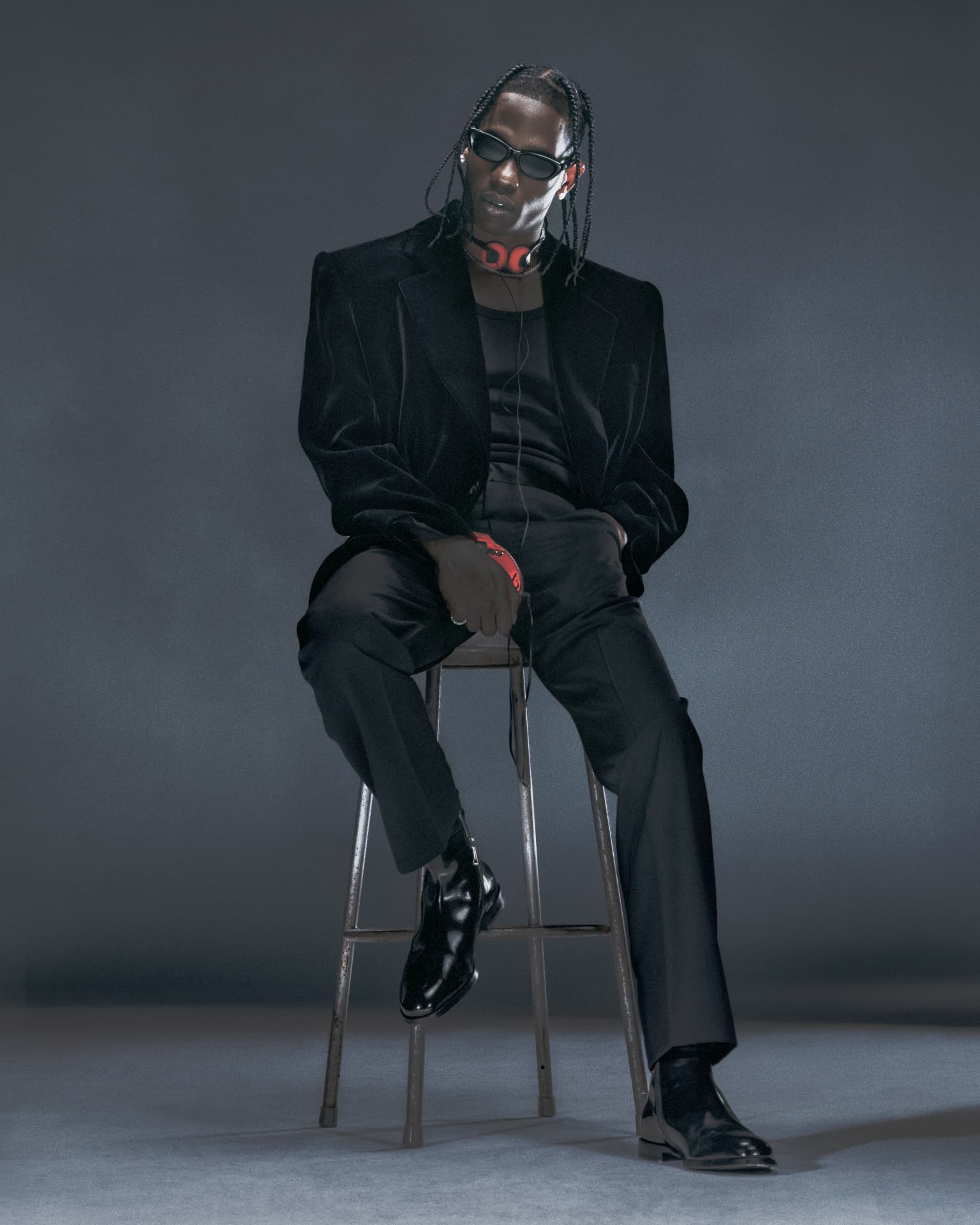 Travis Scott — seated portrait in black suit with red headphones and sunglasses