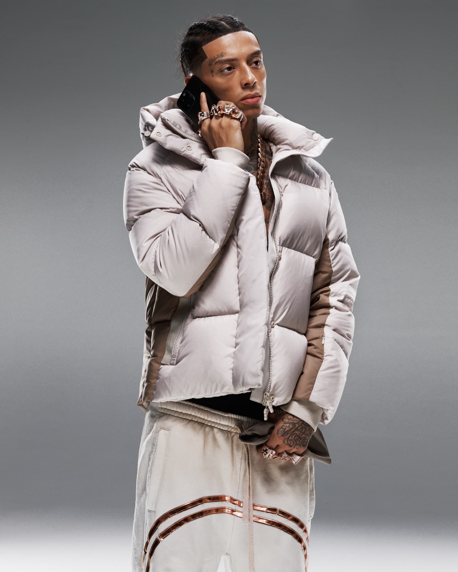 Central Cee — portrait in light grey puffer jacket on phone with CANT RUSH rings