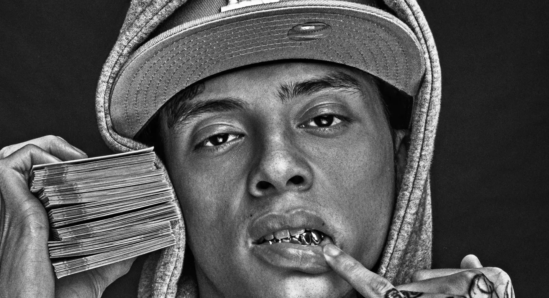 Black and white portrait with cap, grill, and stack of bills