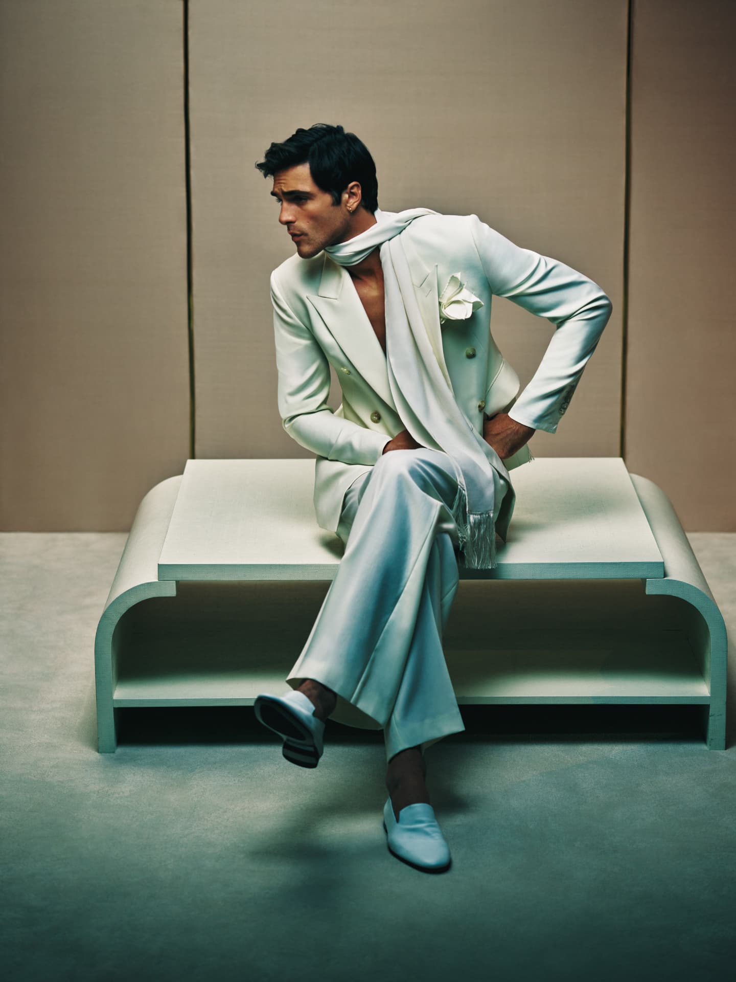 Jacob Elordi — seated on a white bench in cream suit with scarf