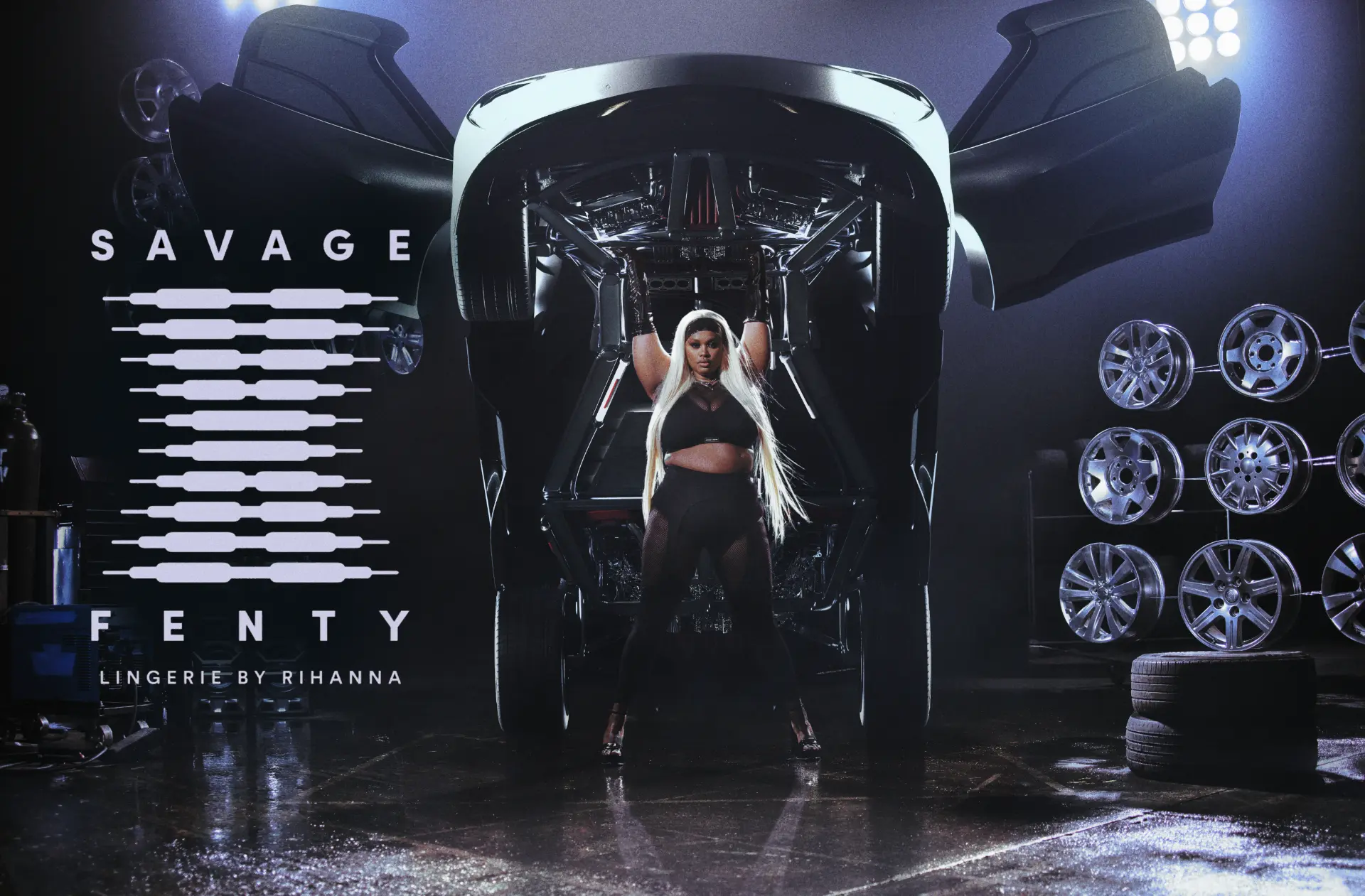 Savage x Fenty — figure beneath a raised car in a garage with logo