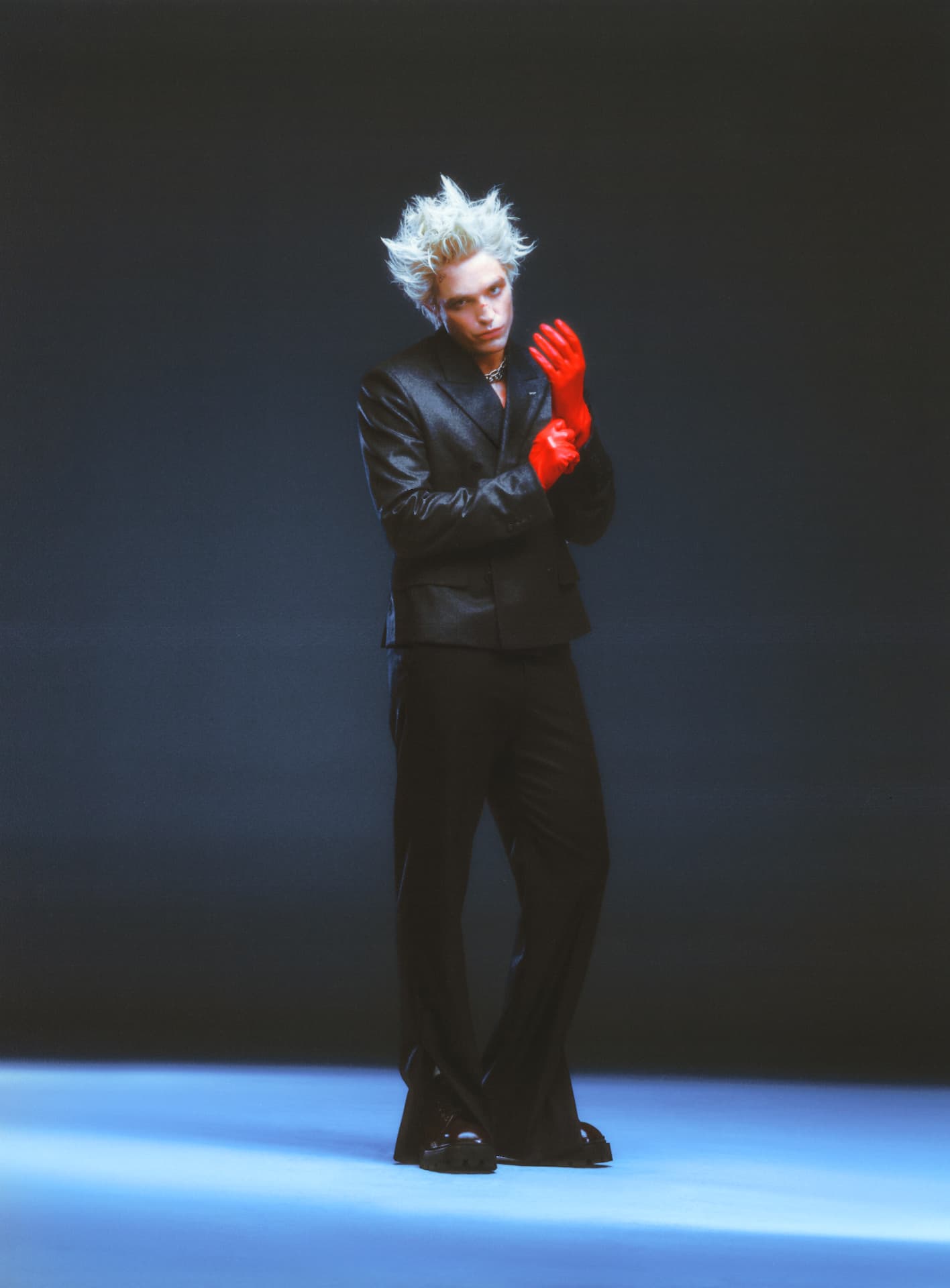 Rob Pattinson GQ — black suit with red gloves against blue backdrop